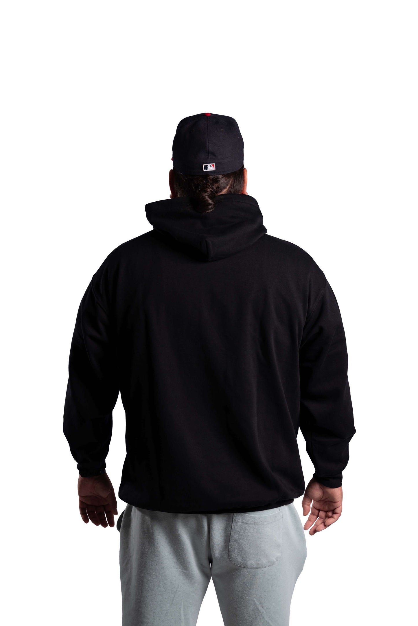 Person wearing a black hoodie and gray pants with a black cap on a white background