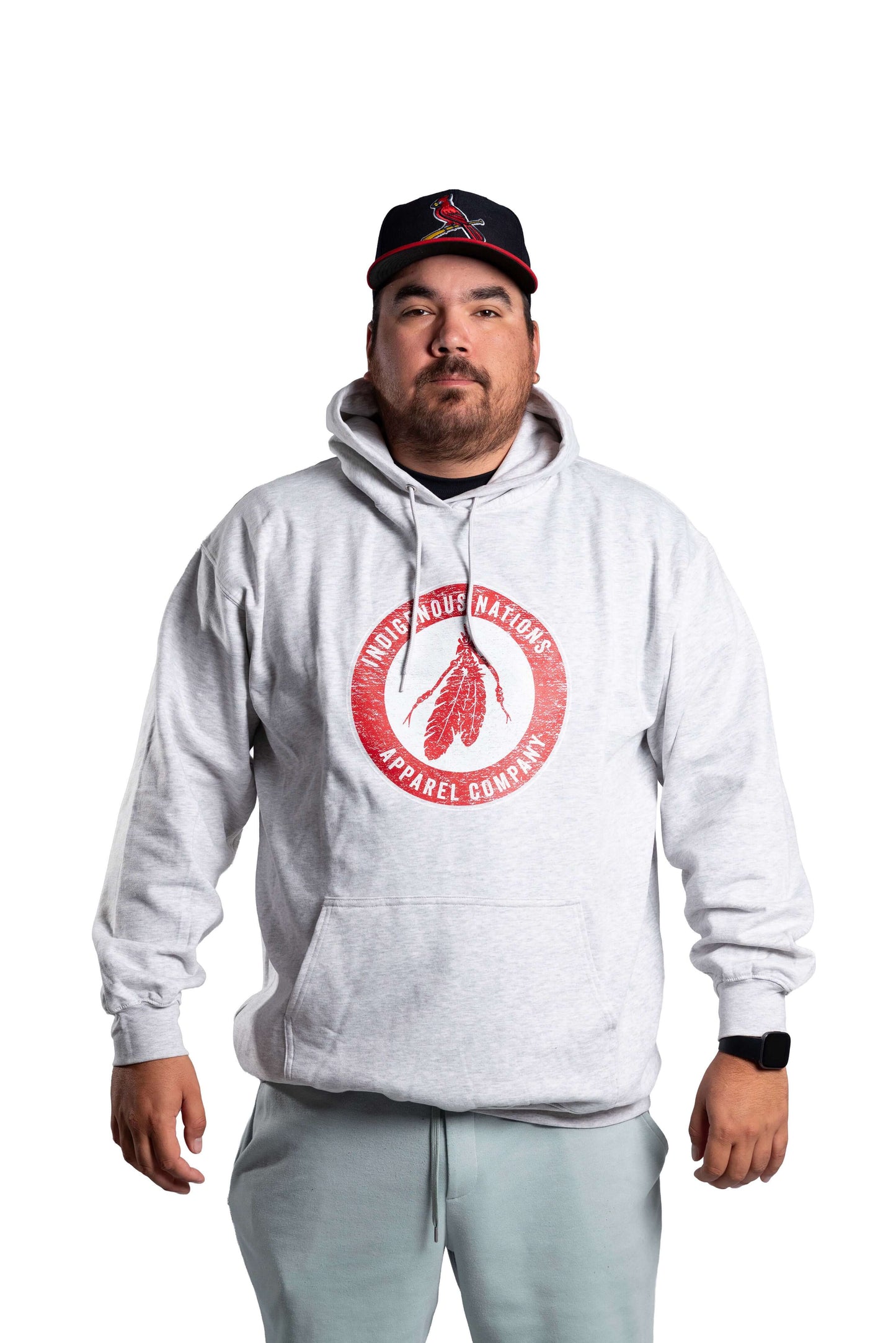 Person wearing a gray hoodie with a red logo and a black cap on a white background