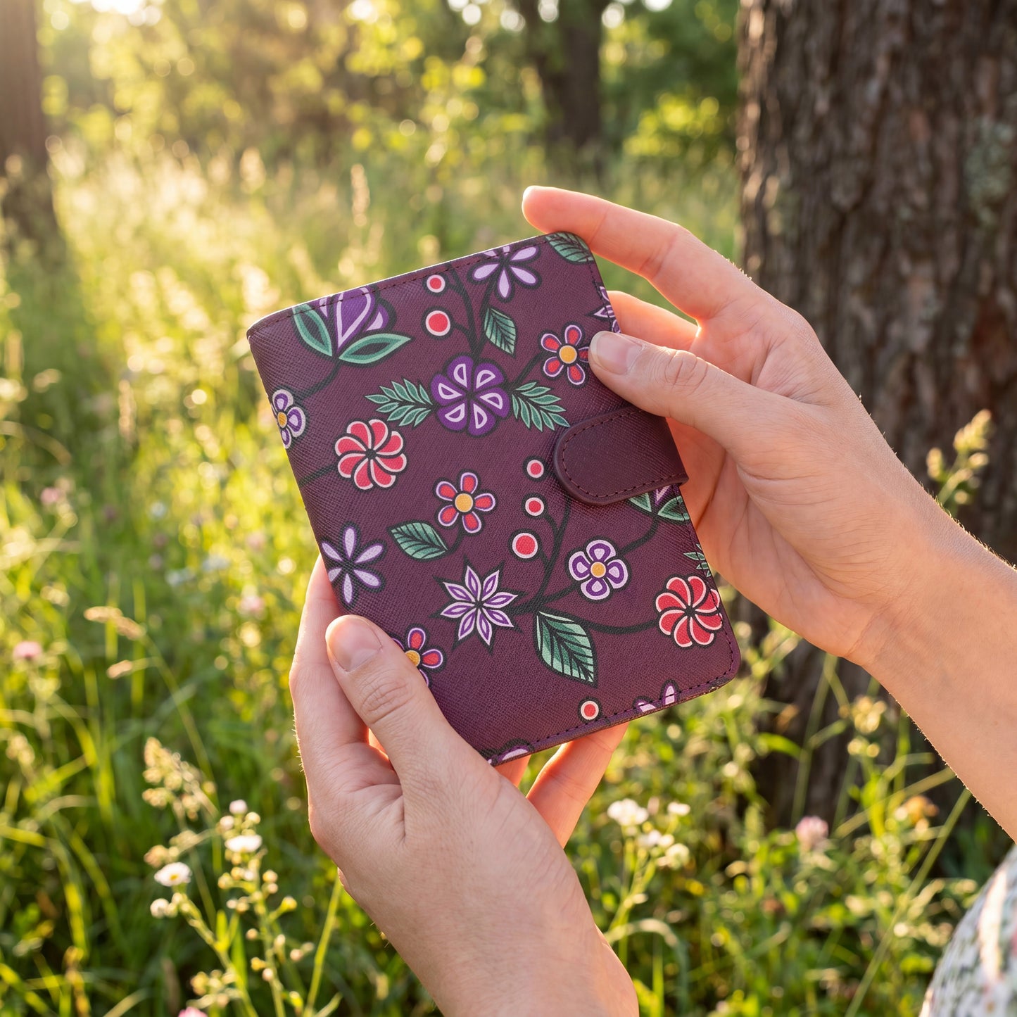 Hand holding a floral-patterned purple wallet in a natural setting with greenery.