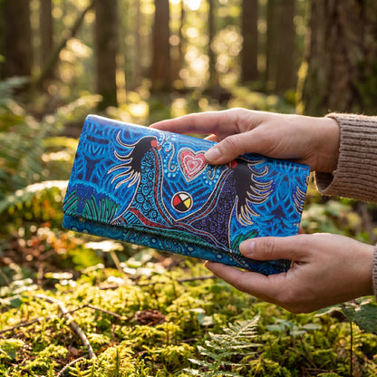 Person holding a blue wallet with a nature-themed design in a forest setting