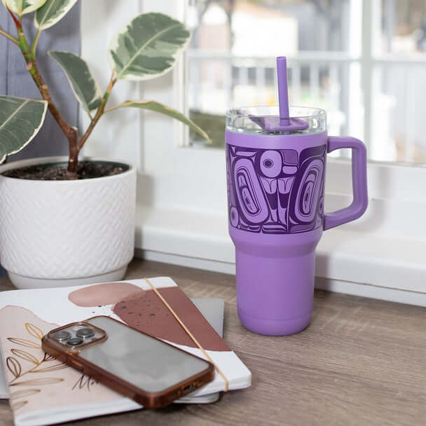 Purple insulated tumbler with butterfly design placed on a desk with books and coffee