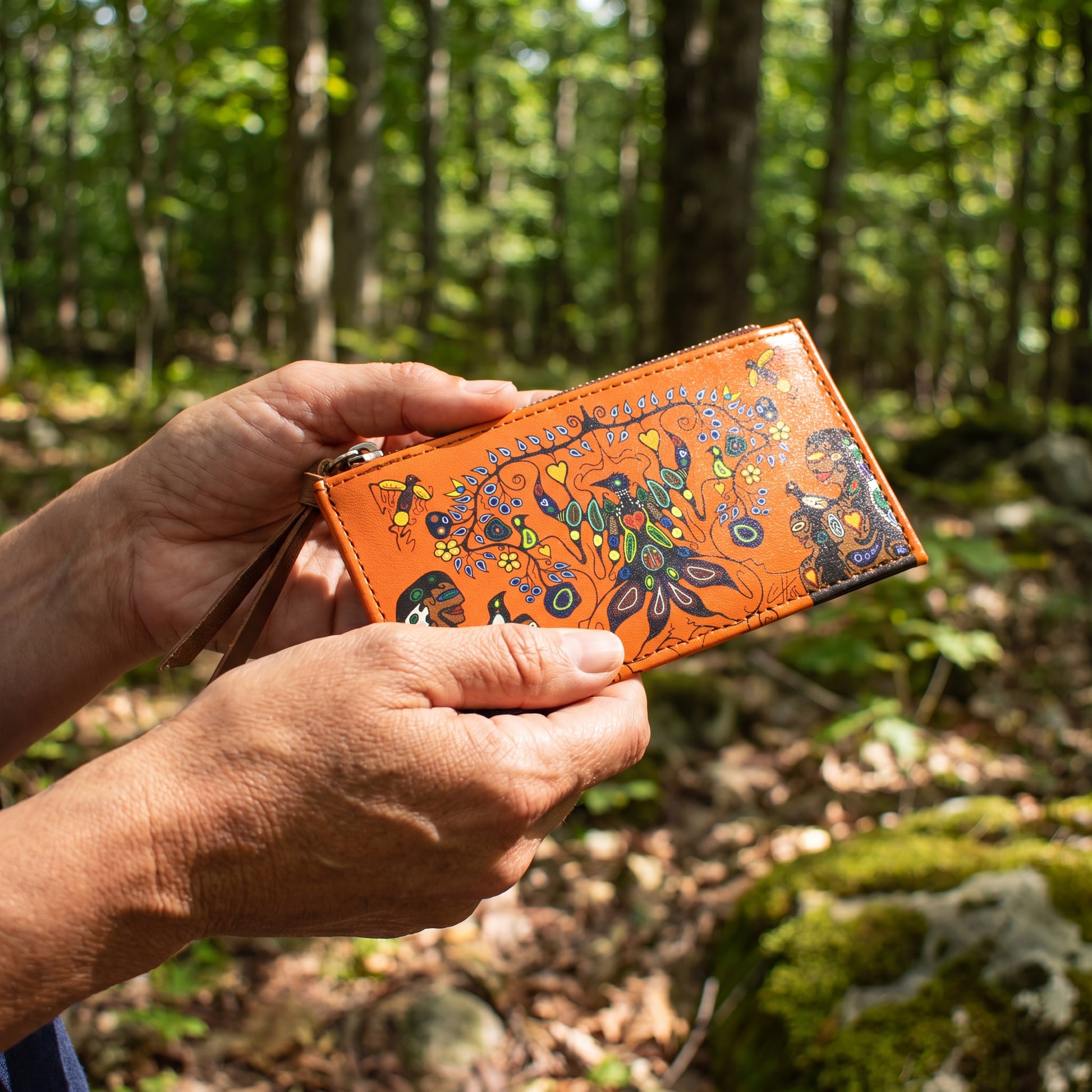 Hand holding a colorful wallet with nature-themed design in a forest setting