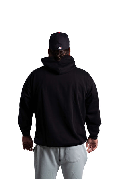 Person wearing a black hoodie and gray pants with a black cap on a white background