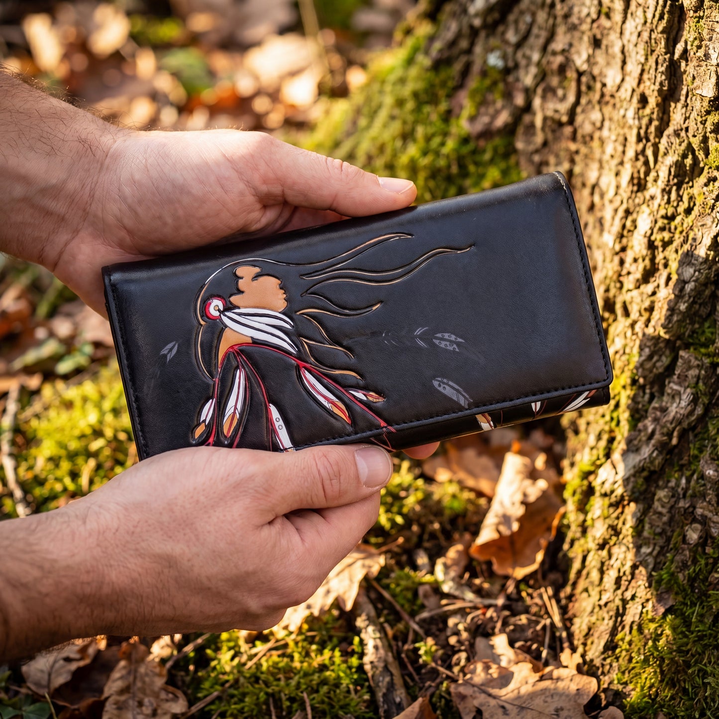 Hand holding a black wallet with a bird design against a natural background