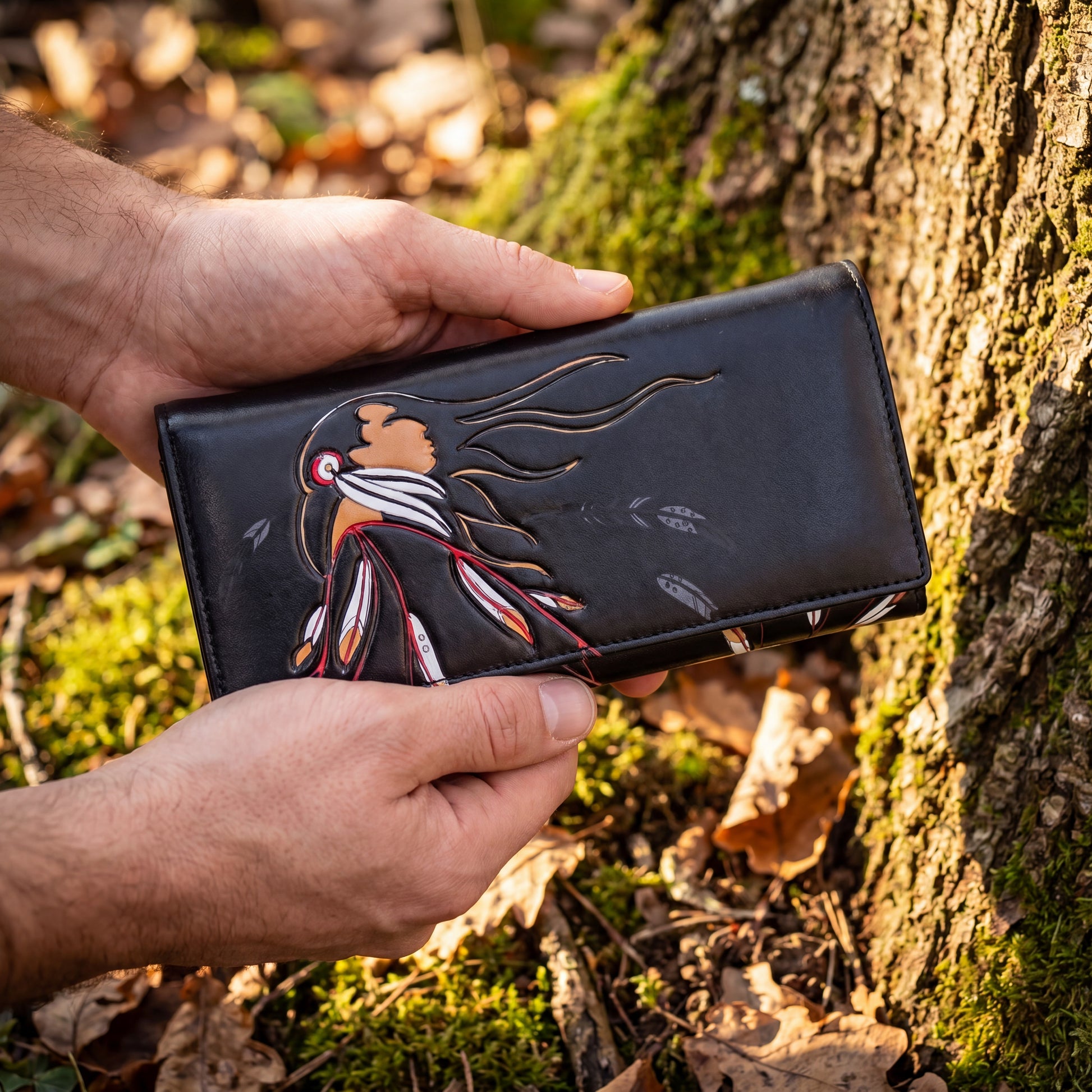 Hand holding a black wallet with a bird design against a natural background