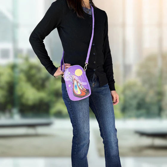 Person wearing a black sweater and blue jeans with a purple crossbody bag featuring a colorful design.