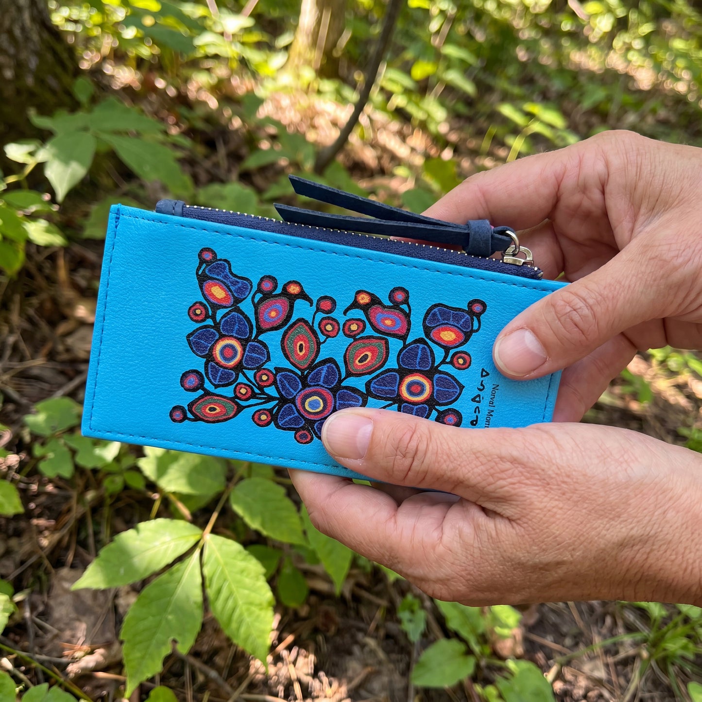 Hand holding a blue pouch with a colorful floral design against a natural background