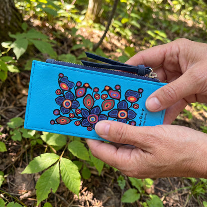 Hand holding a blue pouch with a colorful floral design against a natural background