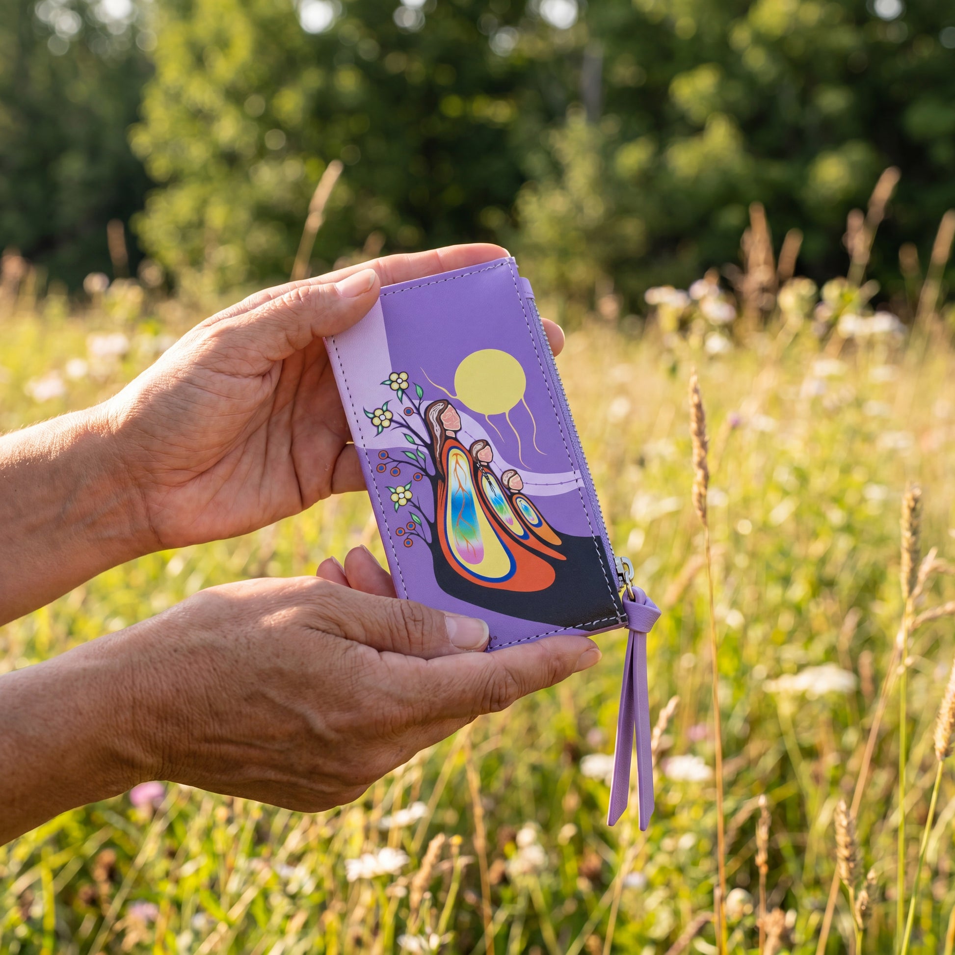 Hand holding a purple wallet with a colorful design against a natural background