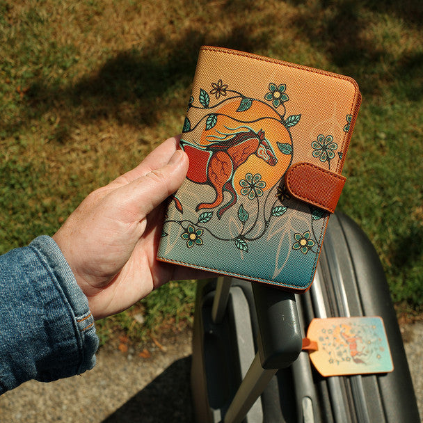 Hand holding a leather wallet with horse design against a blurred outdoor background