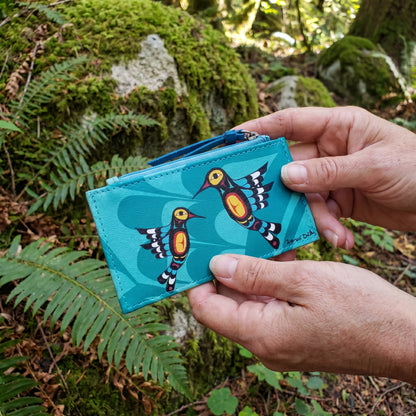 Turquoise cardholder with bird design held by a hand against a natural background