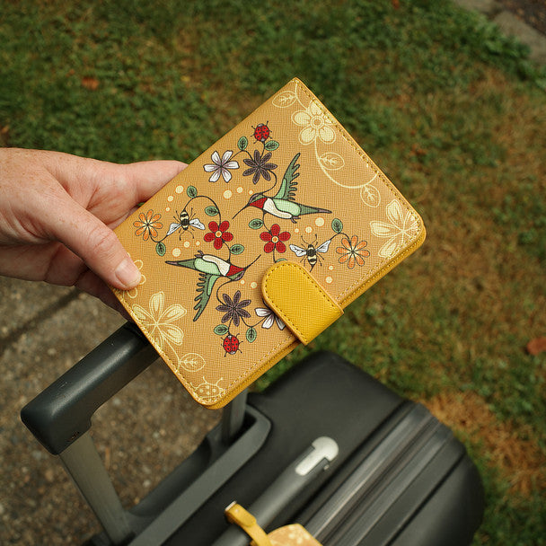 Hand holding a floral-patterned wallet with a suitcase in the background