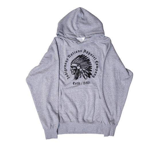 A heather gray pullover hoodie featuring a black circular graphic on the chest with the text 'Indigenous Nations Apparel Company' and 'Estd. 2021' surrounding a profile illustration of a person wearing a feathered headdress.