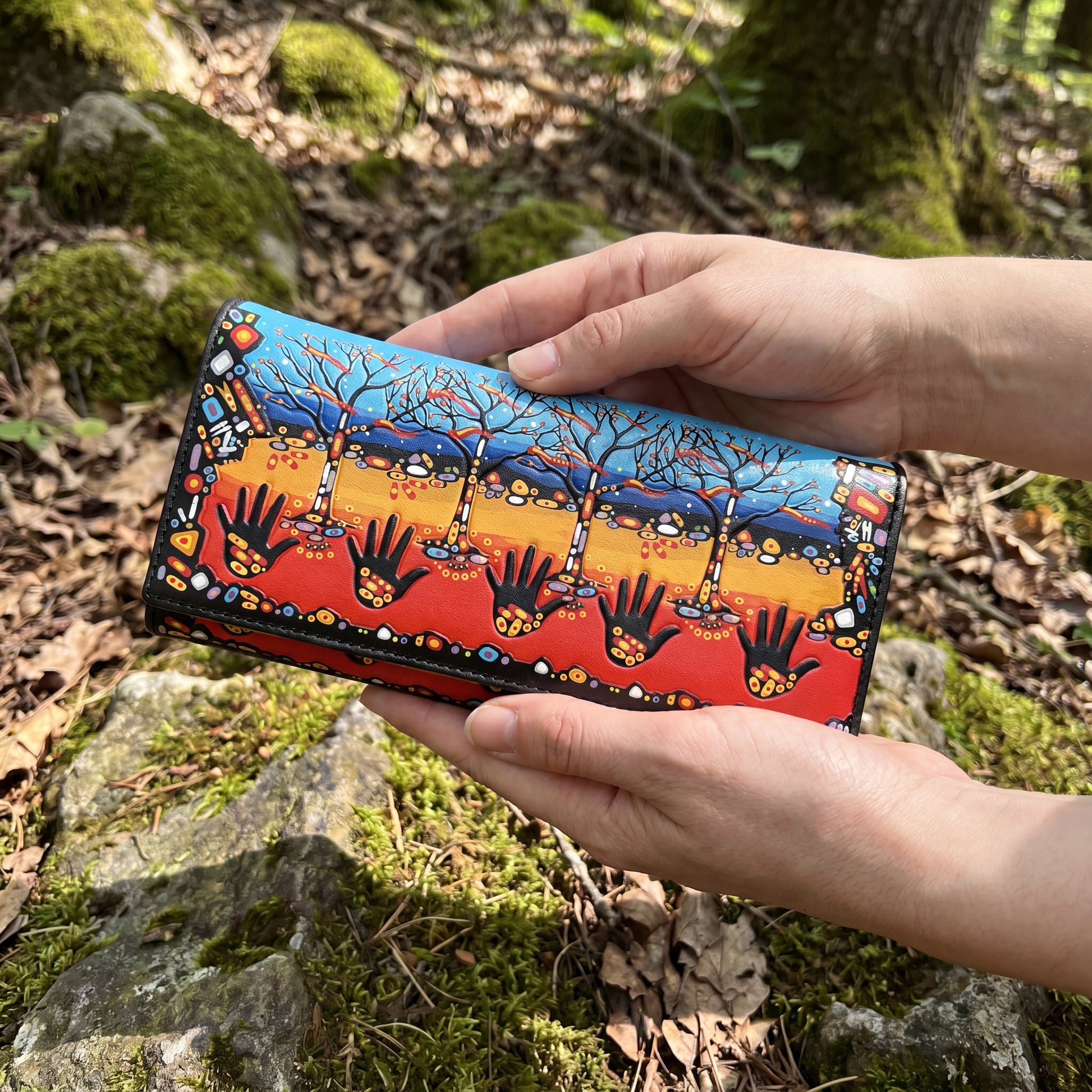 Hand holding a colorful wallet with tree and hand design against a natural background
