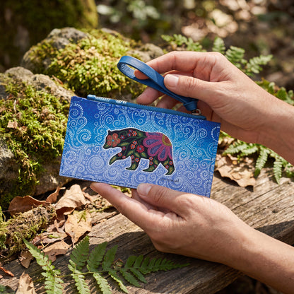 Person holding a blue pouch with a colorful bear design in a natural setting.