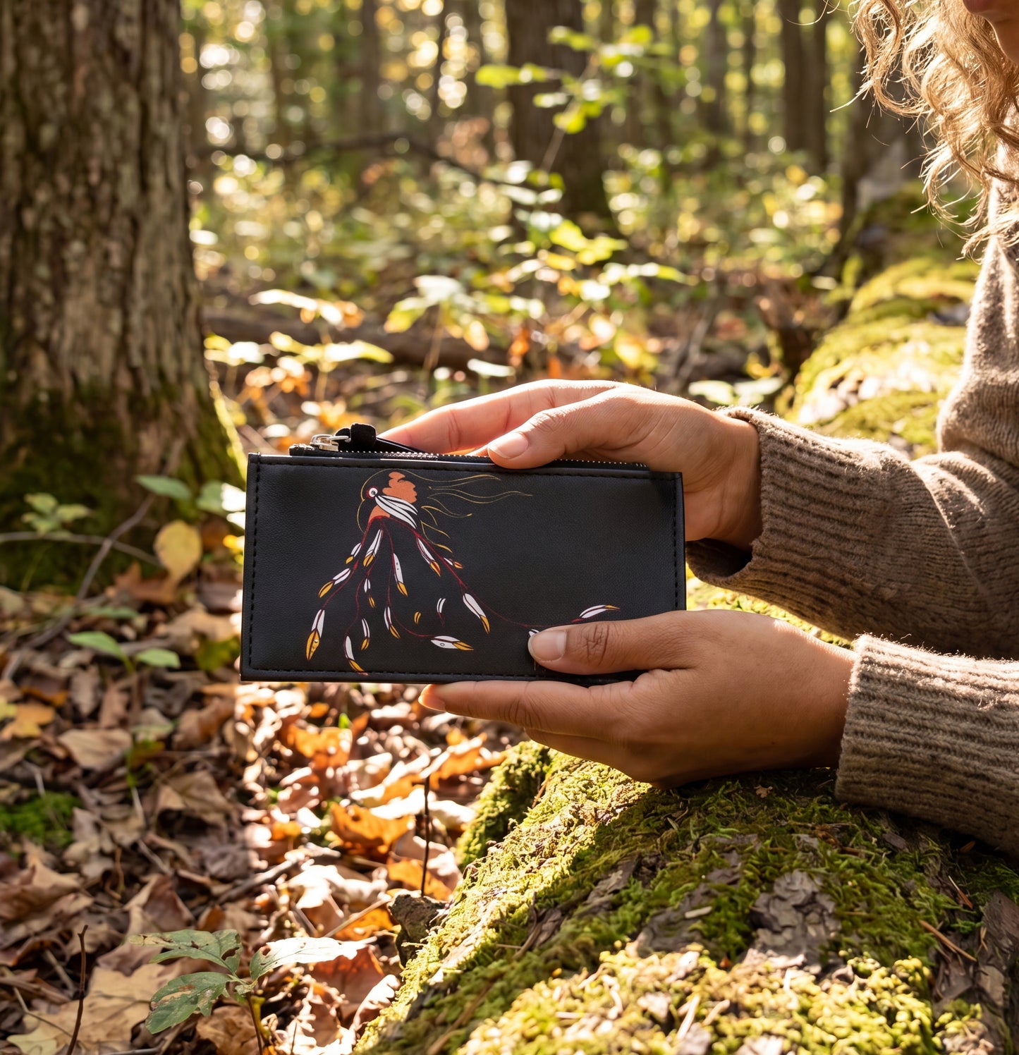 Person holding a black wallet with a colorful design in a forest setting