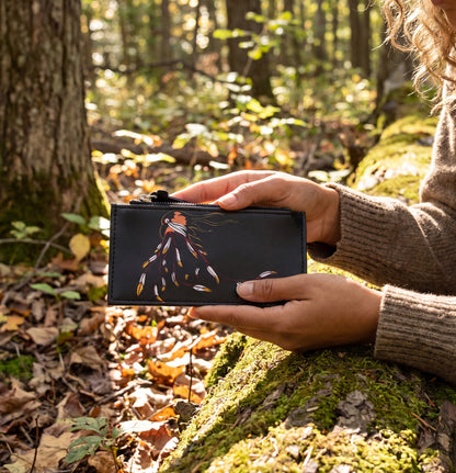 Person holding a black wallet with a colorful design in a forest setting