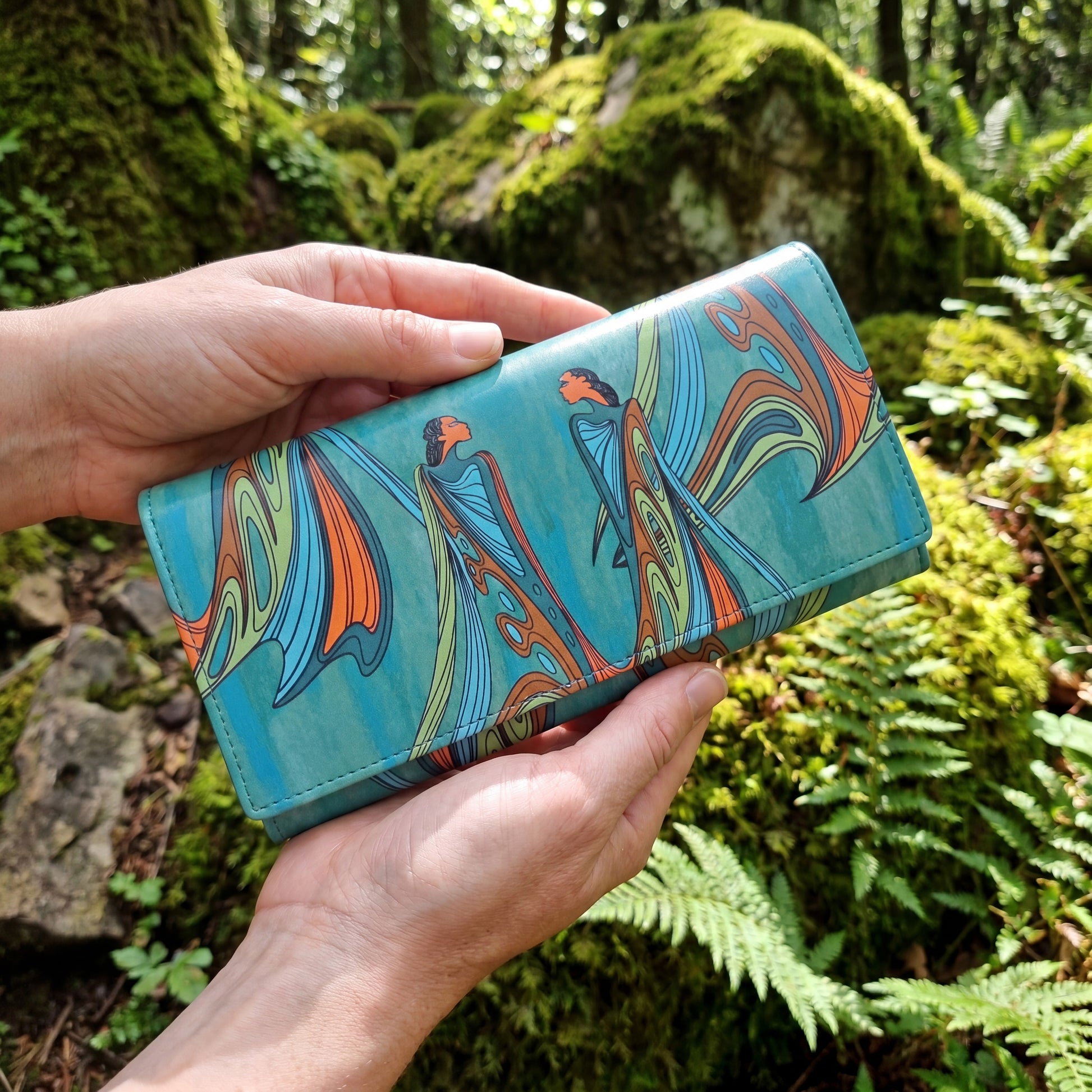 Hand holding a colorful wallet with a nature-themed design against a forest background