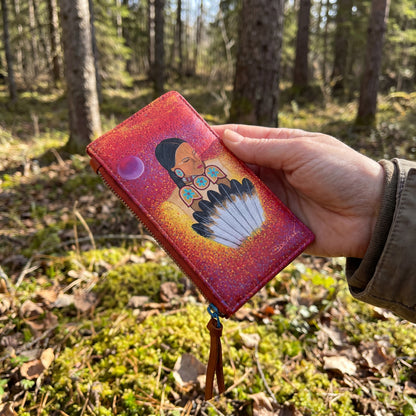 Hand holding a colorful wallet with a Native American design in a forest setting