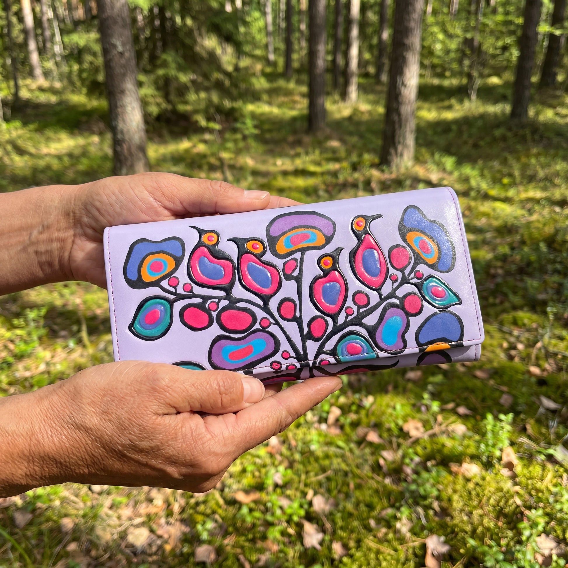 Hand holding a colorful wallet with a floral design against a forest background