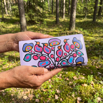 Hand holding a colorful wallet with a floral design against a forest background