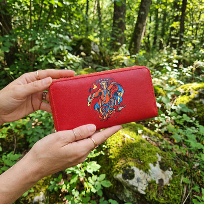 Red wallet with a colorful design held in front of a forest background