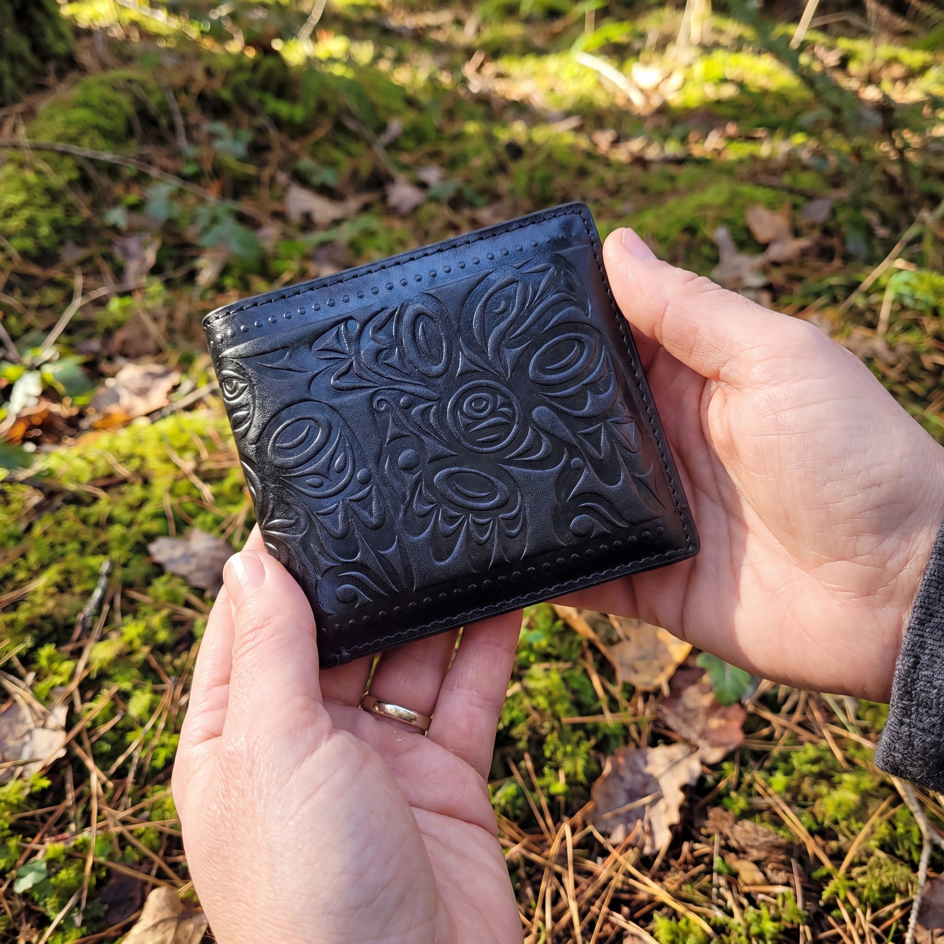 Black embossed wallet held in hands with a natural background