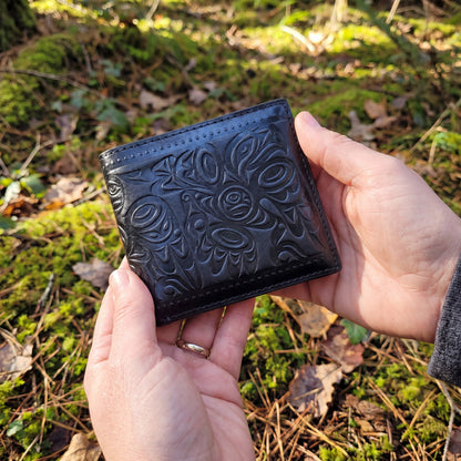Black embossed wallet held in hands with a natural background