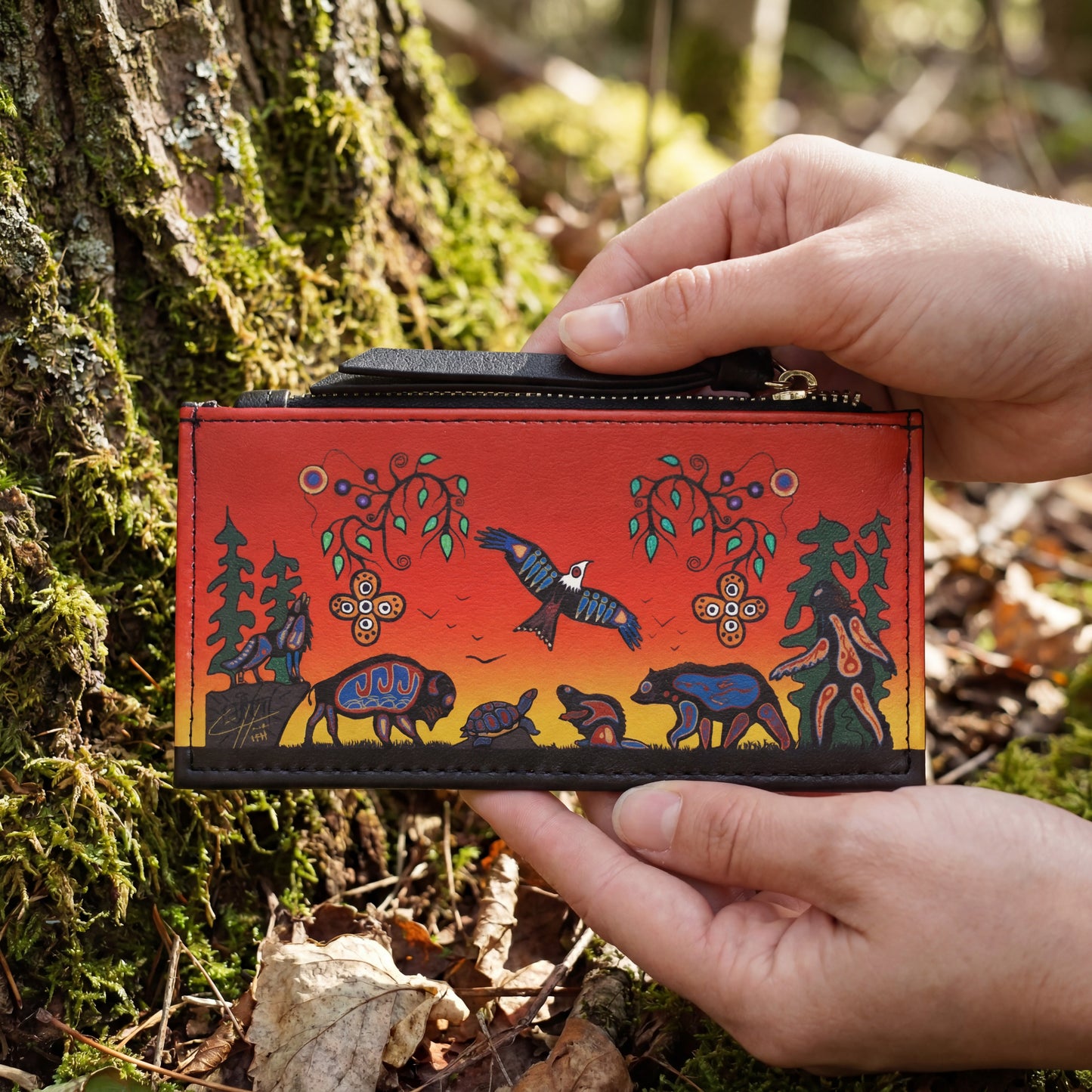 Hand holding a red wallet with nature-themed design against a forest background