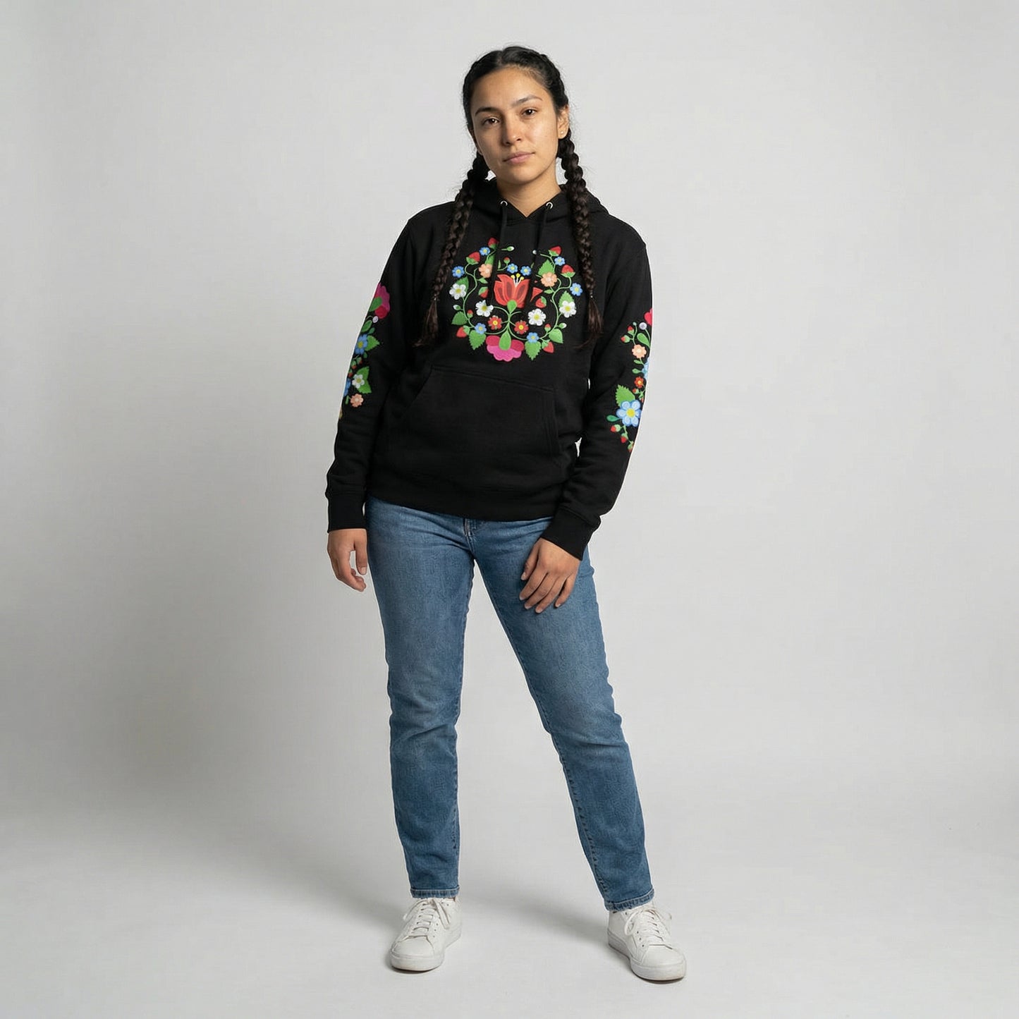 Person wearing a black hoodie with colorful floral design and blue jeans on a plain background