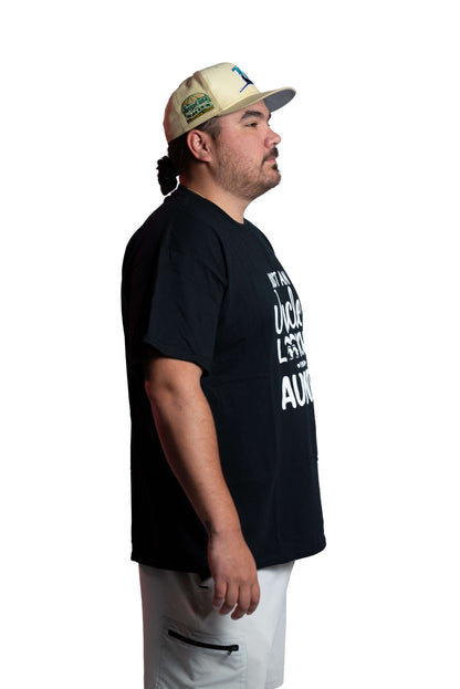 Man wearing a black t-shirt with text and a beige cap on a white background