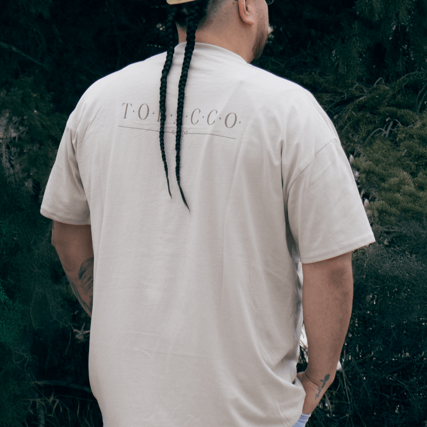 Person wearing Tobacco Medicine Tee in beige Indigenous streetwear graphic shirt back view