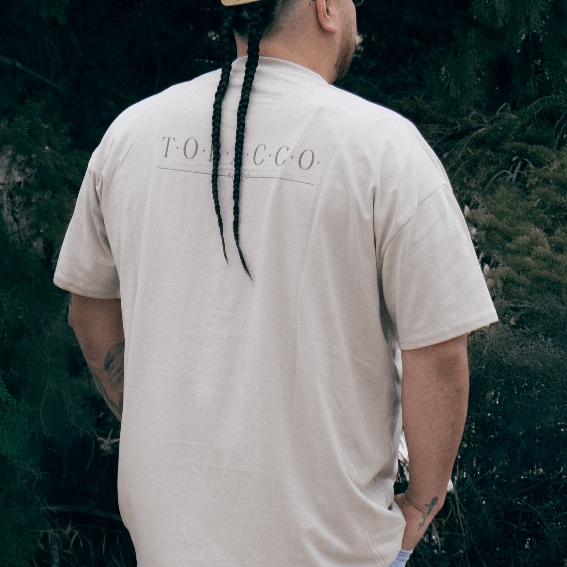 Person wearing Tobacco Medicine Tee in beige Indigenous streetwear graphic shirt back view